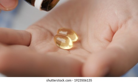 Taking Pills. Two Big Clear Amber Oval Pill Capsules Fall Into Palm Of Hand From Pill Bottle. Close-up, Front View, Center Composition