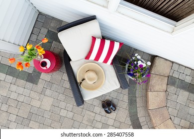 Taking A Relaxing Tea Break In A Deep Seating Patio Set With A Comfortable Armchair Flanked By Colorful Spring Flowers With A Sunhat And Garden Shoes On A Brick Paved Outdoor Patio, Overhead View