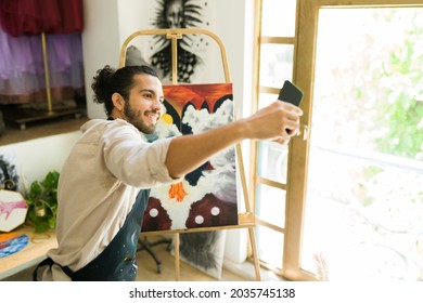 Taking a selfie with my painting. Cheerful latin man posting a picture on social media of his artwork