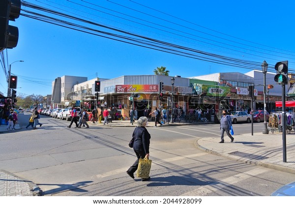 Talca, Maule - Chile - September 03, 2021: crowd walking\
on sidewalk in front of a chinese store in commercial street during\
sunny afternoon. Modern metalic facade of chinese retailing store.\
