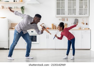 Talented african american young father and little daughter singing songs, standing in the middle of kitchen, holding utensils, making dancing moves, full length shot, copy space - Powered by Shutterstock