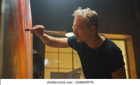 Talented Artist Working on Abstract Painting, Dips Brush in Paint and Starts Drawing Daringly Emotional Modern Art. Dark Creative Studio Large Canvas Stands on Easel Illuminated - Powered by Shutterstock