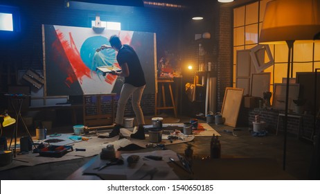 Talented Artist Working on Abstract Painting, Uses Tray Palette to Mix Colors and Paint Brush To Create Daringly Emotional Modern Picture. Dark Creative Studio Large Canvas Stands on Easel Illuminated - Powered by Shutterstock