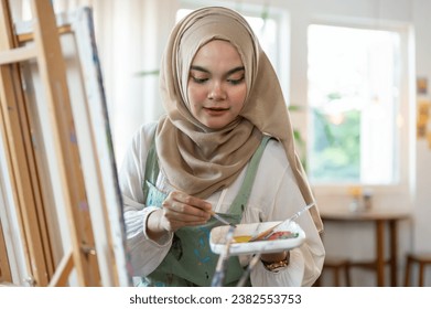 A talented Asian-Muslim female artist focuses on painting on canvas, mixing colors on a palette, working in her home studio. - Powered by Shutterstock