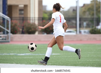 Talented athletic high school aged female soccer player dribbling the ball down the field, or pitch during a competitive game of soccer - Powered by Shutterstock