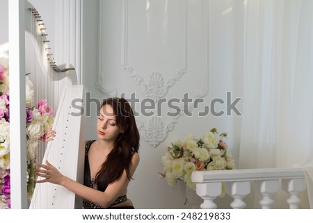 Talented attractive young female musician playing the harp on a fresh white stage during a recital or musical concert