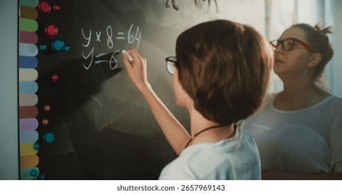 Talented Boy Demonstrating Math Knowledge: Close Up Shot of Primary School Student Solving Mathematical Equation Writing on the Board with Chalk in Classroom. Female Teacher Checking Correct Answers.