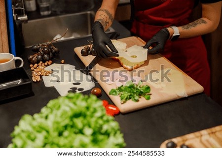 A talented chef skillfully assembles a gourmet sandwich, artfully using a variety of fresh vegetables and cheeses