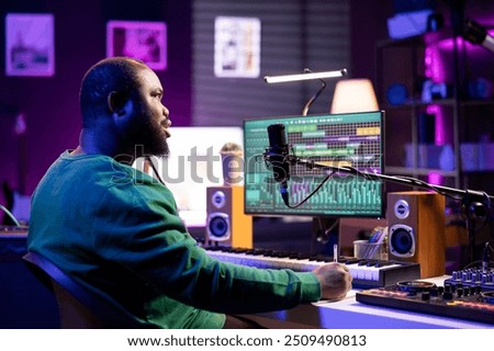 Talented famous composer writes down new verses and lyrics in home studio, composing new music with digital software. Artist songwriter works with audio equipment and gear, recording tracks.