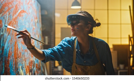 Talented Female Artist Wearing Augmented Reality Headset Working on Abstract Painting, Uses Paint Brush To Create New Concept Art Using Virtual Reality Interface. High tech Creative Modern Studio