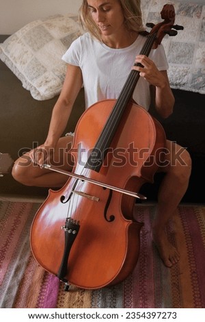 Talented female musician with fiddlestick sitting on couch and playing melody on cello in living room at home on weekend day