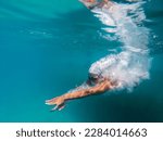 A talented female swimmer dives into a full-size tournament pool to train or compete. This stunning wide-angle underwater photo captures the grace and power of this athlete in action.