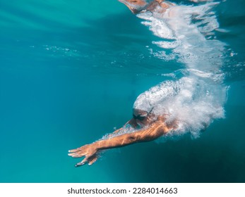 A talented female swimmer dives into a full-size tournament pool to train or compete. This stunning wide-angle underwater photo captures the grace and power of this athlete in action. - Powered by Shutterstock