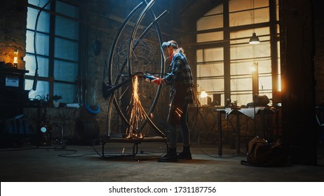 Talented Innovative Female Artist Walks Up to a Metal Tube Sculpture, Turns On and Uses an Angle Grinder in a Workshop. Contemporary Fabricator Creating Modern Steel Art. - Powered by Shutterstock