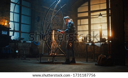 Talented Innovative Female Artist Walks Up to a Metal Tube Sculpture, Turns On and Uses an Angle Grinder in a Workshop. Contemporary Fabricator Creating Modern Steel Art.