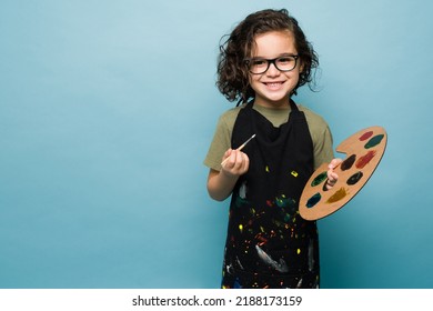 Talented kid smiling using an apron and paintining while dreaming of becoming a famous painter artist