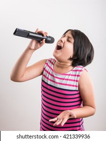 A talented little Indian girl singing on mic, on white studio background.  lovely asian girl holding a black wireless microphone and singing