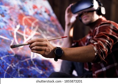 Talented male artist wearing virtual reality headset in creative modern studio. Artist works on abstract oil painting. Abstract Modern Art.