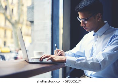 Talented Male Student Of Literature Faculty Of University Making Researchers For Best Annual Book Due To Rating On Internet Users Writing Report In Notebook While Searching Information Via Laptop