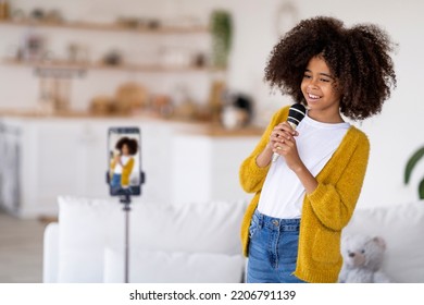 Talented Preteen Black Girl Singing Karaoke At Home, Recording Video For Followers, Child Singer Performing Online, Using Cell Phone On Tripod, Holding Microphone, Copy Space