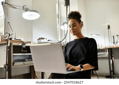 A talented woman types on her laptop in a jewelry workshop, showcasing creativity and dedication. - Powered by Shutterstock