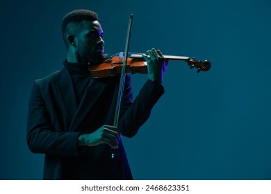 Talented young African American man playing violin with passion and skill against a dark blue background - Powered by Shutterstock