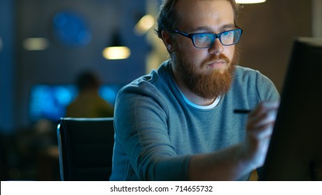 Talented Young Concept Artist Drawing On A Digital Pen Display Tablet While Sitting At His Working Place In Modern Loft Office. Late At Night.