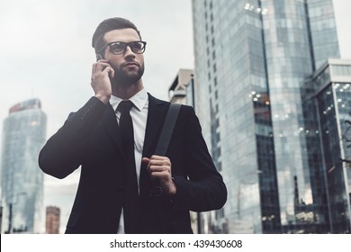 Talking about business. Confident young man in full suit talking on the mobile phone and looking away while standing outdoors with cityscape in the background - Shutterstock ID 439430608