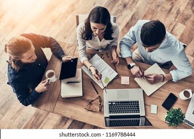 Talking About Business Details. Top View Of Young Modern Colleagues In Smart Casual Wear Working Together While Spending Time In The Office