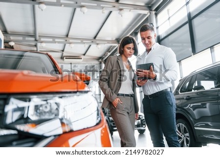 Talking with each other. Man in formal wear helping customer with choice of the automobile.