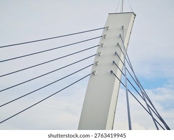 Tall angled bridge pylon with multiple steel cables radiating outward, set against a blue sky with light clouds.