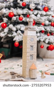 Tall architectural model of a clock tower made from miniature ceramic bricks. The construction features a dome, arched windows, and a small side building, presented in a festive home setting with a Christmas tree in the background.

Высокая архитектурная модель башни с часами, выполненная из миниатюрных керамических кирпичиков. Постройка включает в себя купол, арочные окна и небольшую пристройку, представленная в праздничной домашней обстановке на фоне новогодней елки.
