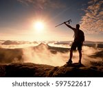 Tall backpacker with poles in hand. Sunny misty daybreak in rocky mountains. Hiker with backpack stand on rocky view point above valley. Vivid and strong vignetting effect.