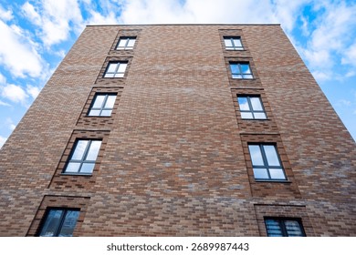 A tall brick building with rectangular windows, decorated in warm tones, set against a clear blue sky with light clouds. A modern and austere architectural style.