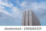 A tall building against a background of blue, cloudy sky. The building is very tall and has many windows.