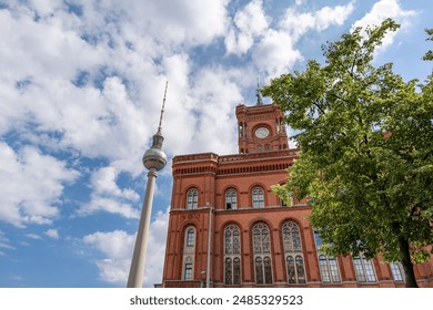 A tall building with a clock tower and a tall television tower. The sky is blue and there are clouds in the background. - Powered by Shutterstock