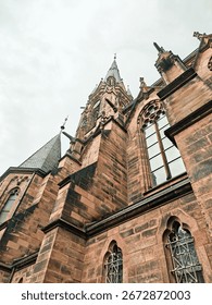A tall building with a clock tower and a tree in front of it in Saarbrucken Germany. The sky is cloudy and the building is white