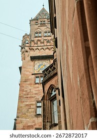 A tall building with a clock tower and a tree in front of it in Saarbrucken Germany. The sky is cloudy and the building is white