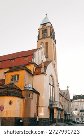 A tall building dominates the view. Structures display varied architectural details. Roofs feature red tiles. Windows are numerous. The sky appears overcast - Plzen, Czech - Jan,19,2026