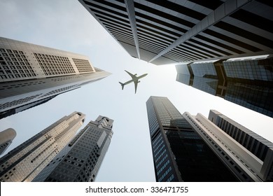 Tall City Buildings And A Plane Flying Overhead