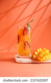 tall cocktail glass filled with yellow juice and fresh strawberries and cut in cubes mango half on tropical orange background, gobo mask effect - Shutterstock ID 2157625307