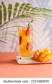 tall cocktail glass filled with yellow juice and fresh strawberries and cut in cubes mango half on tropical palm tree background - Shutterstock ID 2157683935
