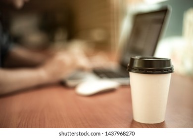 A Tall Coffee Cup In Front Of A Man Working On A Laptop Computer.