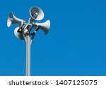 A tall column with four gray loudspeakers in a circle against a clean blue sky. Hazard warning system. The possibility of placing your test or image.