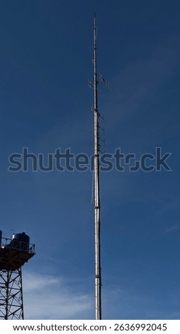 Tall Communication Tower Against Clear Blue Sky, A towering metal communication antenna stands prominently against a vibrant blue sky, symbolizing modern technology and connectivit.