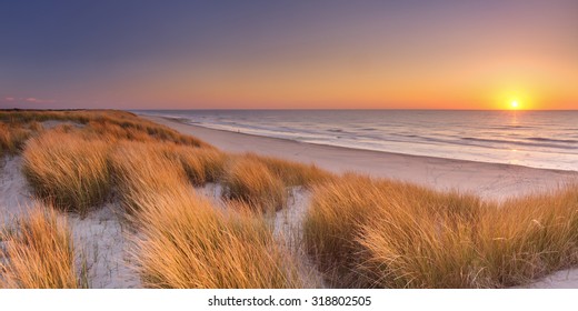 Tall dunes with dune grass and a wide beach below. Photographed at sunset on the island of Texel in The Netherlands. - Powered by Shutterstock