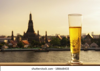 Tall glass of beer  with The background is a view of Wat Arun, Landmark in Bangkok.