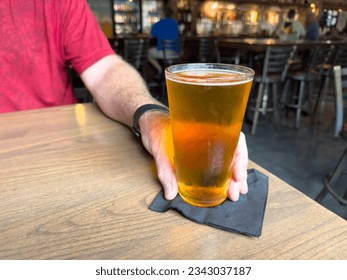 A tall glass of cold craft beer with a thick head of white froth. The Irish red ale beer glass is on the edge of a wooden table at a brewery.  The gold alcohol refreshment beverage of draft beer.     - Powered by Shutterstock