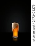 Tall glass filled with amber colored lager beer, topped with creamy white head against black studio background. Concept of alcohol drinks, summer, traditions, Oktoberfest. Ad