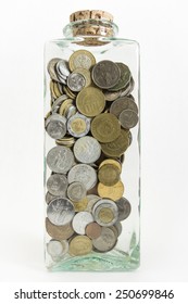A tall glass jar with stopped with a cork and filled with international coins from New Zealand, Costa Rica, Mexico, Europe, Canada, and the United States.